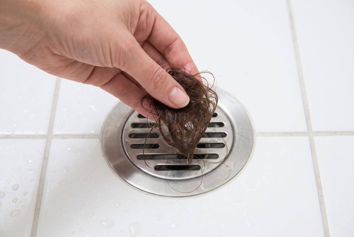 A hand pulling a clump of shed hair out of a shower drain