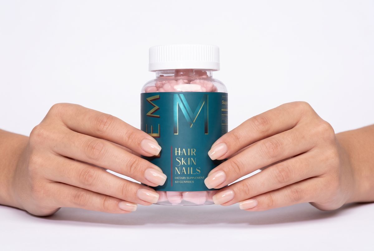 Two hands with strong, glossy natural nails holding a jar of WEEM Hair Skin Nails gummies