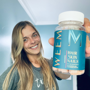 Person smiling and holding a bottle of WEEM Hair, Skin, and Nails supplement.